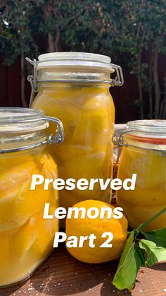 jars filled with lemons sitting on top of a wooden table next to green leaves