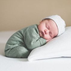 a newborn baby sleeping on top of a white pillow wearing a green sweater and knitted hat