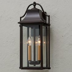 two candles are lit in an old fashioned lantern on the side of a white wall