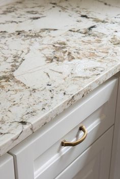 a marble counter top in a kitchen with brass handles on the cabinet doors and drawers