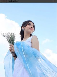 a woman wearing a white dress holding a blue scarf over her shoulder and looking up at the sky