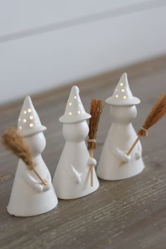 three small white ceramic christmas trees with lights on their heads and one is holding a broom