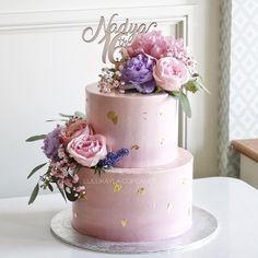 a three tiered cake with pink and purple flowers on the top, sitting on a table