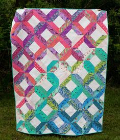 a colorful quilt on the grass with trees in the background