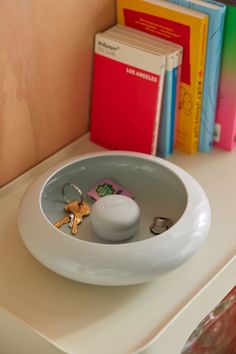 there is a white bowl with keys in it on the counter next to some books