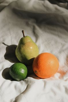 three different types of fruit sitting on a white sheet with one green apple and two oranges