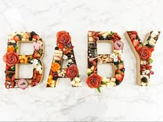 the word baby spelled out in letters made from fruits and veggies on a white marble surface