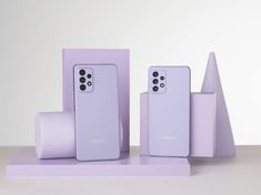 two samsung phones are sitting on display in front of some other devices, one is purple and the other is white