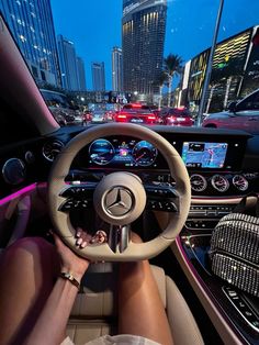 a woman is driving in the city at night with her hands on the steering wheel