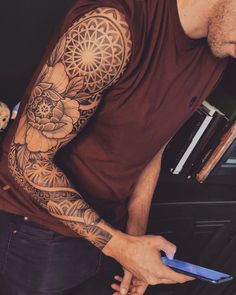 a man with a flower tattoo on his arm holding a cell phone and looking down