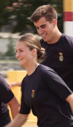 two young people are walking together in black t - shirts, smiling at each other