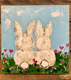 a painting of two rabbits sitting in the grass with flowers and hearts painted on it