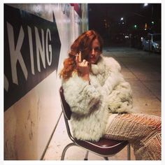 a woman is sitting on a chair talking on her cell phone while leaning against a wall