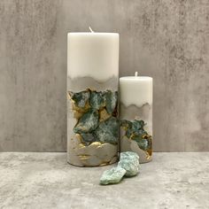 two candles sitting next to each other on top of a marble table with green rocks