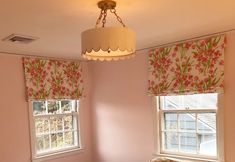 a bedroom with pink walls and floral roman shades on the window sill, along with a bed