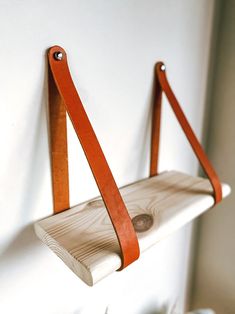 a wooden shelf with two leather straps hanging from it's sides on a white wall