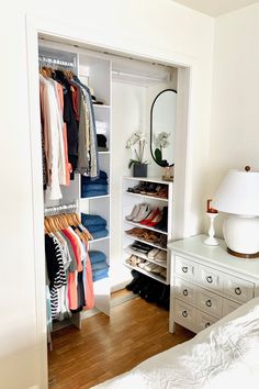 an open closet with clothes and shoes on the shelves next to a bed in a bedroom