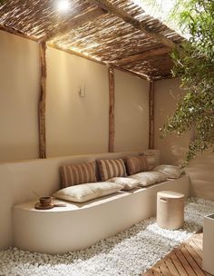 a bed sitting under a bamboo roof next to a plant in a room with white pebbles on the floor