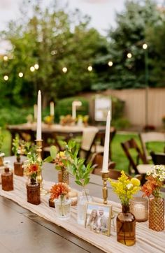 a long table with candles and vases on it in the middle of a yard