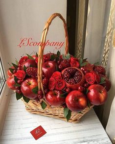 a basket filled with apples and flowers on top of a table next to a window