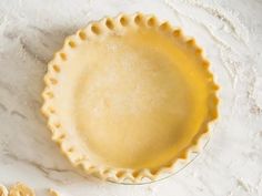 an uncooked pie crust sitting on top of a white marble countertop next to some cut up cookies