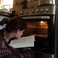 a woman reading a book in front of an oven