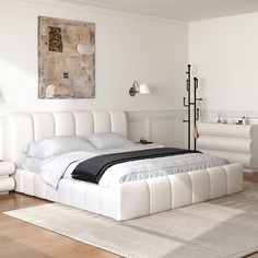 a large white bed sitting on top of a hard wood floor next to a painting