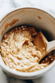 a bowl filled with peanut butter on top of a marble counter next to a wooden spoon