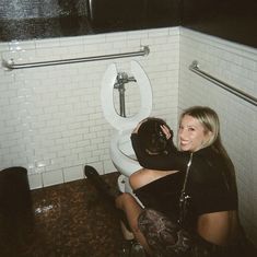 a woman sitting on the floor in front of a toilet with her arm around a man's head