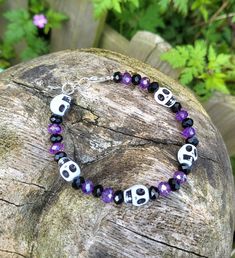 a bracelet with skulls and purple beads is sitting on top of a wooden rock in the grass