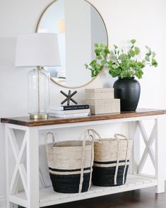 two baskets sit on top of a table next to a mirror and vase with plants in it