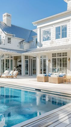 a large white house with a pool in the foreground and two lounge chairs on the other side