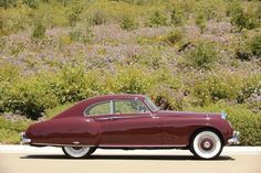 an old car is parked on the side of the road in front of some bushes