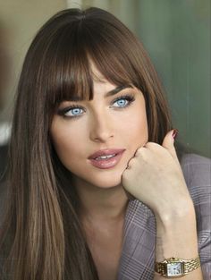 a woman with long brown hair and blue eyes wearing a watch on her left wrist