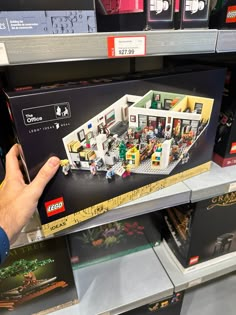 a hand is holding up a lego house in a store shelf with other items on the shelves