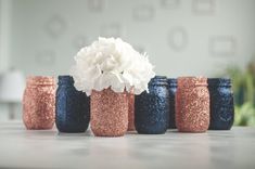 five blue and pink vases with white flowers in them sitting on a countertop