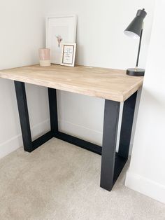 a wooden desk with black legs and a lamp next to it on carpeted floor