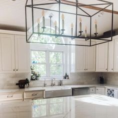 Above a spacious white marble island hangs a black framed candelabra chandelier with eight bulbs. The kitchen is draped in cream with stainless steel appliances. Where the metal frame attaches to the ceiling, there are exposed brown ceiling beams with white panels to display the elegant vaulted ceiling...   Image: thevintagebreadbox