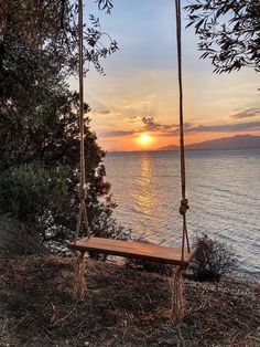 a wooden bench sitting on top of a lush green hillside next to the ocean at sunset