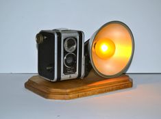 an old fashioned camera sitting on top of a wooden stand next to a yellow light