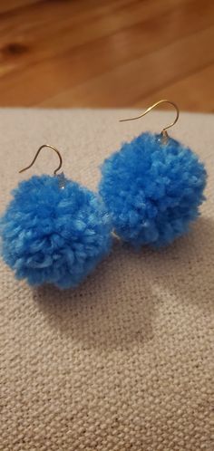 the blue pom - pom earrings are hanging from gold earwires on a piece of fabric