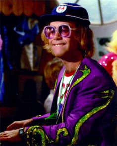 a man wearing sunglasses and a purple jacket sitting in front of a stuffed animal doll