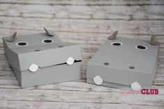 two boxes with holes in them sitting on a wooden table, one is grey and the other is white