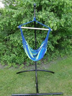 a blue hammock hanging from a metal stand in the grass with trees behind it