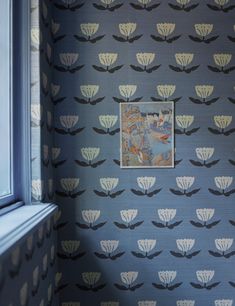 a wallpapered room with a painting on the window sill and blue walls