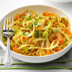 a white bowl filled with noodles, meat and veggies next to a fork