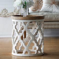 a white vase with flowers sitting on top of a wooden table next to a couch