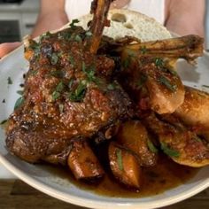 a person holding a plate with some meat and potatoes on it in front of the camera