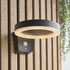 an outdoor light mounted on the side of a wooden wall next to a potted plant