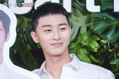 the young man is wearing a white shirt and posing in front of a green wall